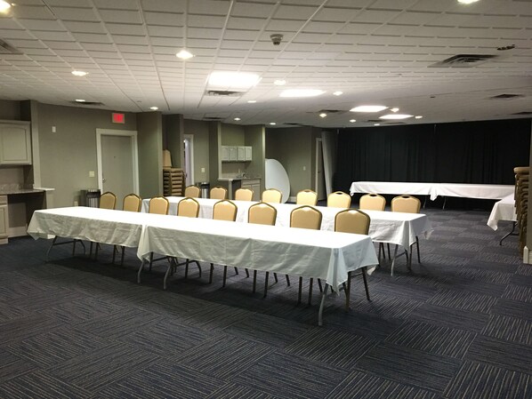Un salón de conferencias con varias mesas y sillas, una kitchenette y una zona para presentaciones.