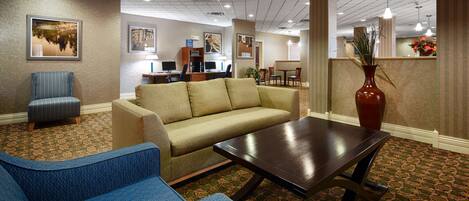 A hotel lobby with a sofa, chairs, a coffee table, and a reception desk.
