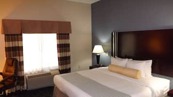 A hotel room with a bed, a chair, a nightstand with a lamp, and a window with curtains.