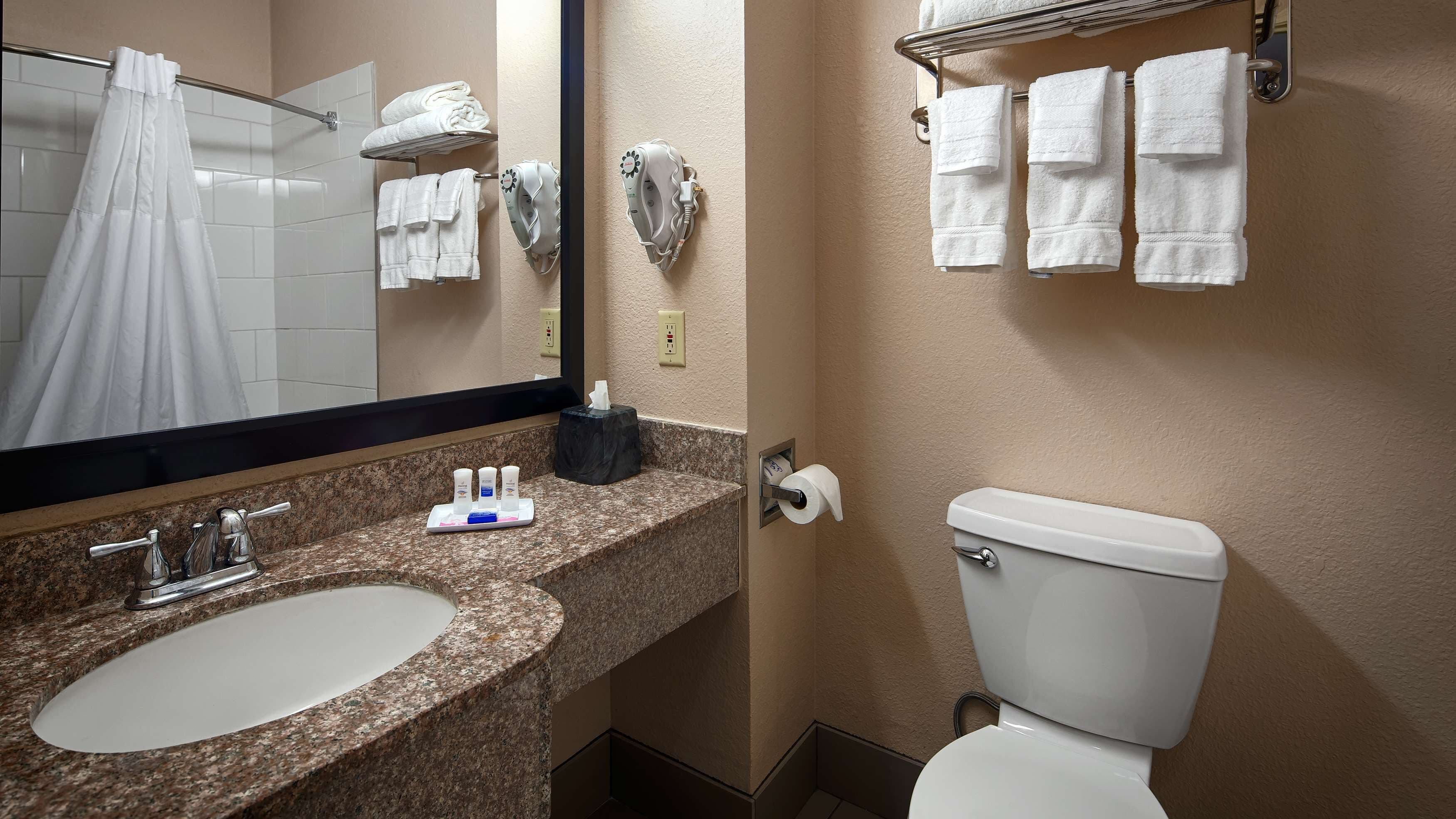 A bathroom with a sink, mirror, towel rack, toilet, and a towel dispenser.