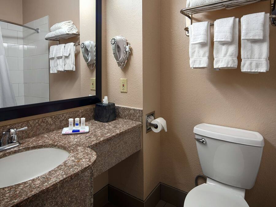 Un baño con lavamanos, espejo, toallero, inodoro y dispensador de toallas.