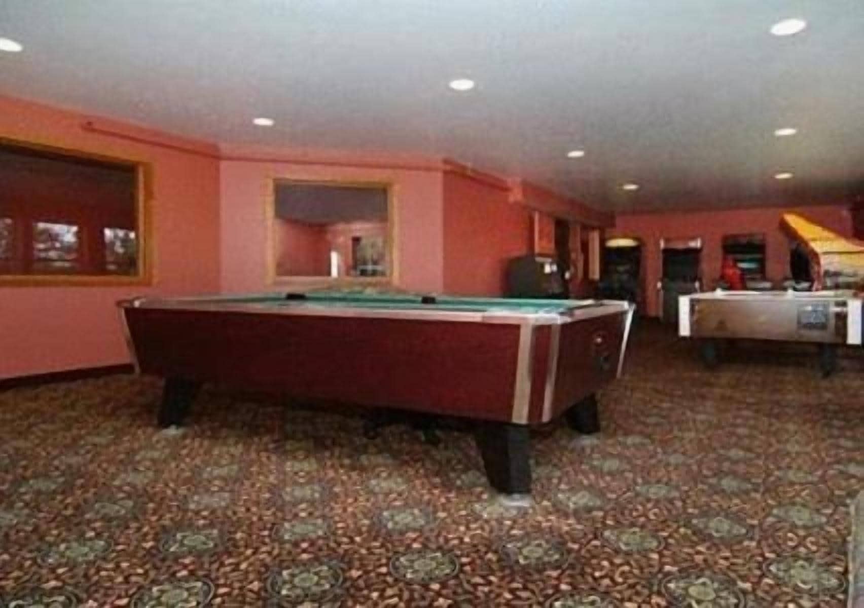 A pool table in a room with patterned carpet and pink walls.
