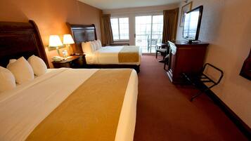 A hotel room with two beds, a desk, a television, and a balcony with a view.