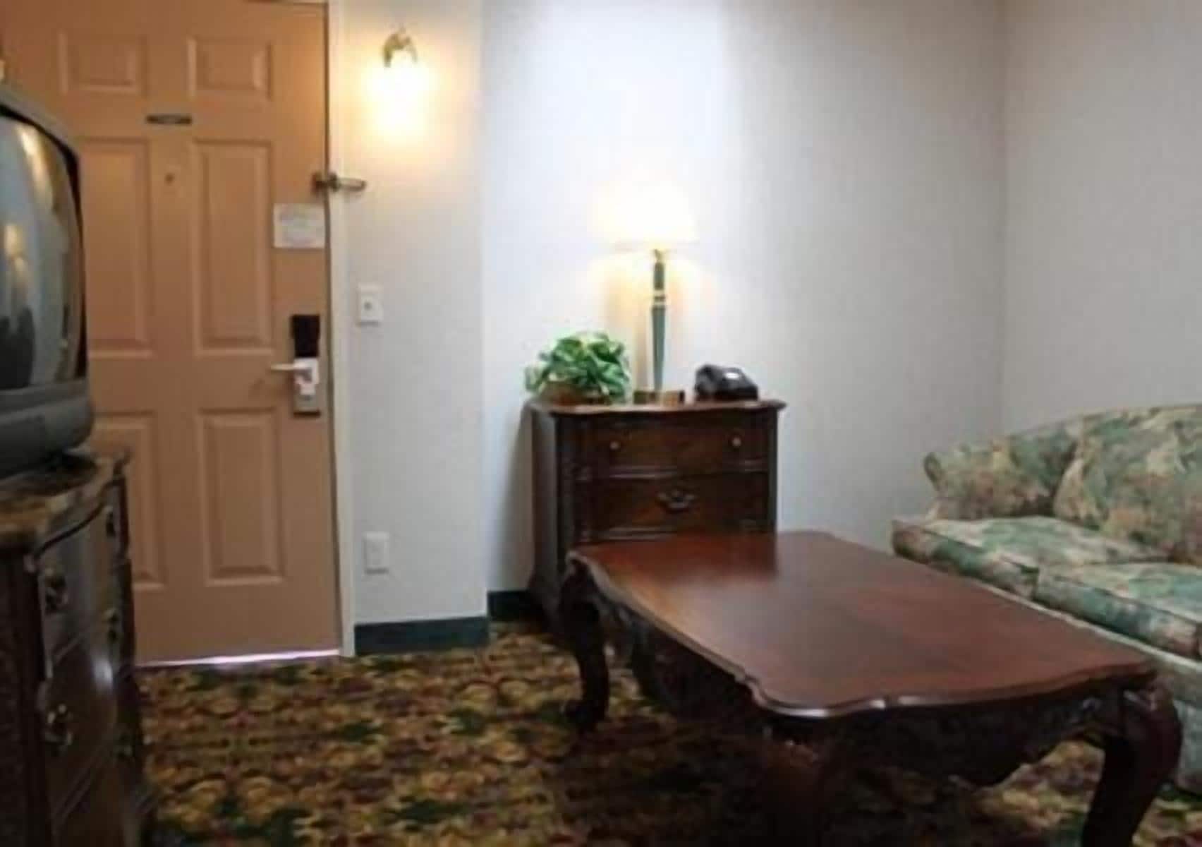 A room with a wooden coffee table, a sofa, a lamp, and a television on a stand.