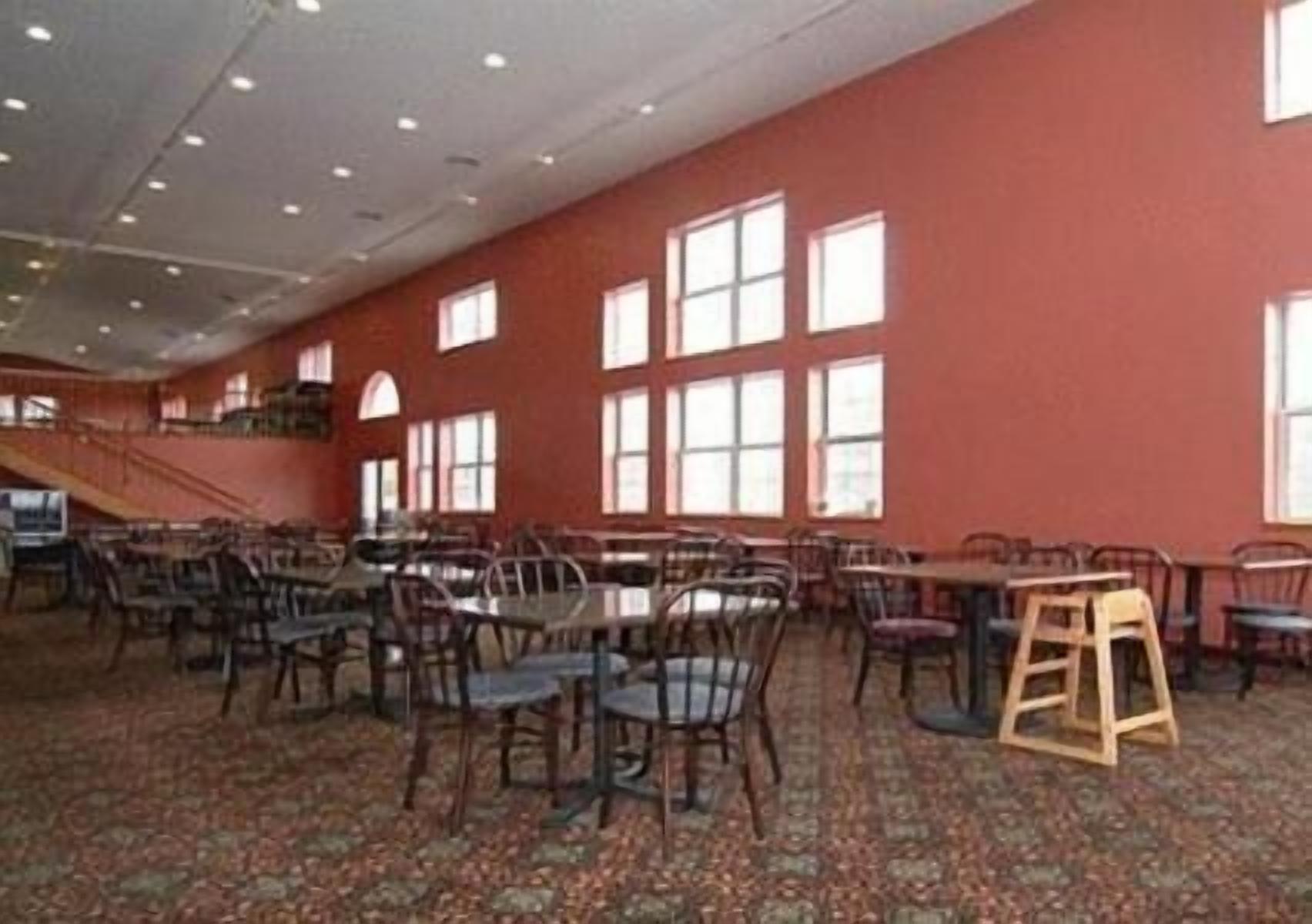 A spacious room with multiple tables and chairs, large windows, and a carpeted floor.