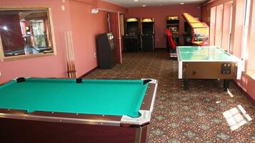 A pool table, a foosball table, and arcade machines in a room with patterned carpet and pink walls.