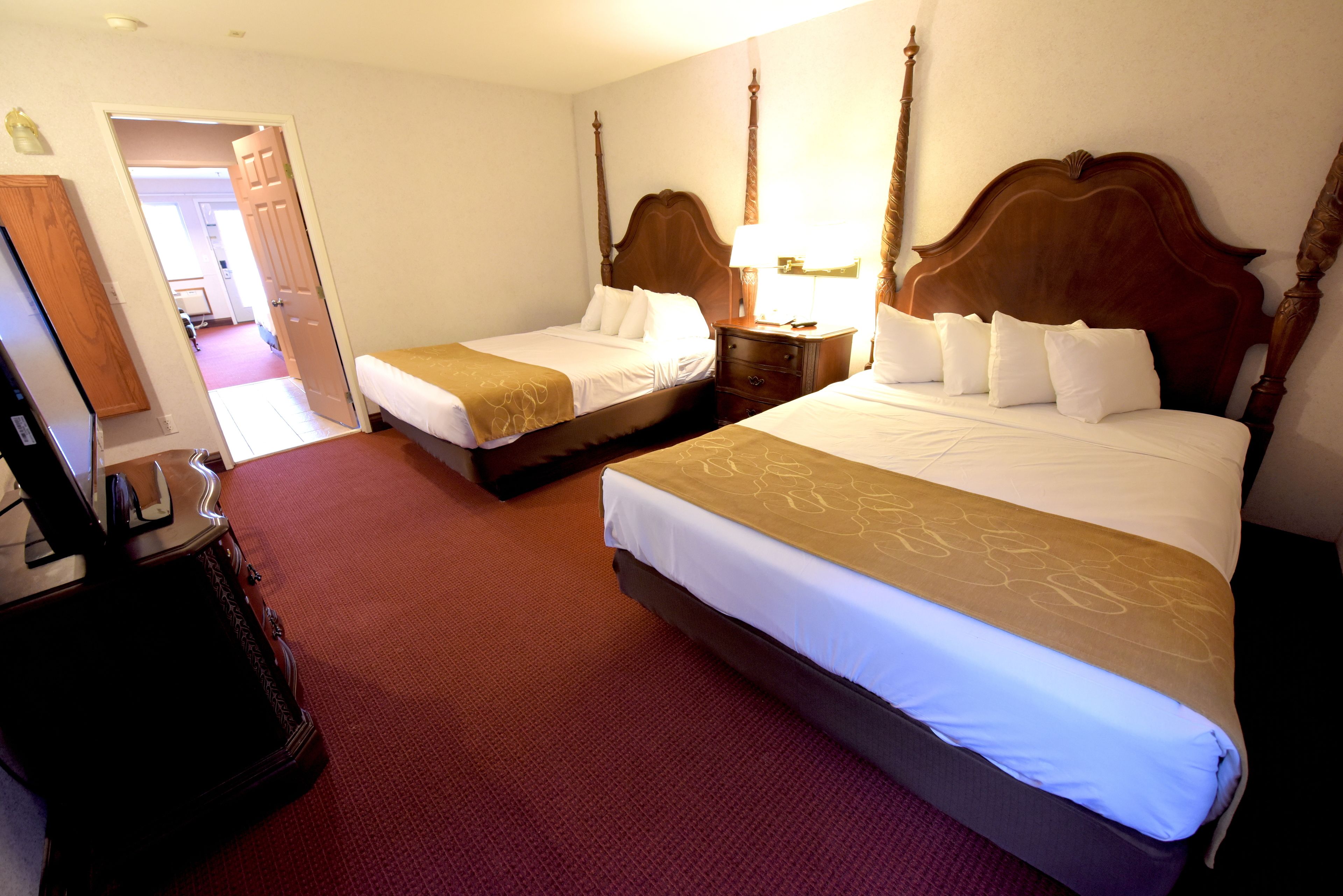 Hotelkamer met twee bedden, een houten hoofdbord, een nachtkastje met een lamp en een rood tapijt.
