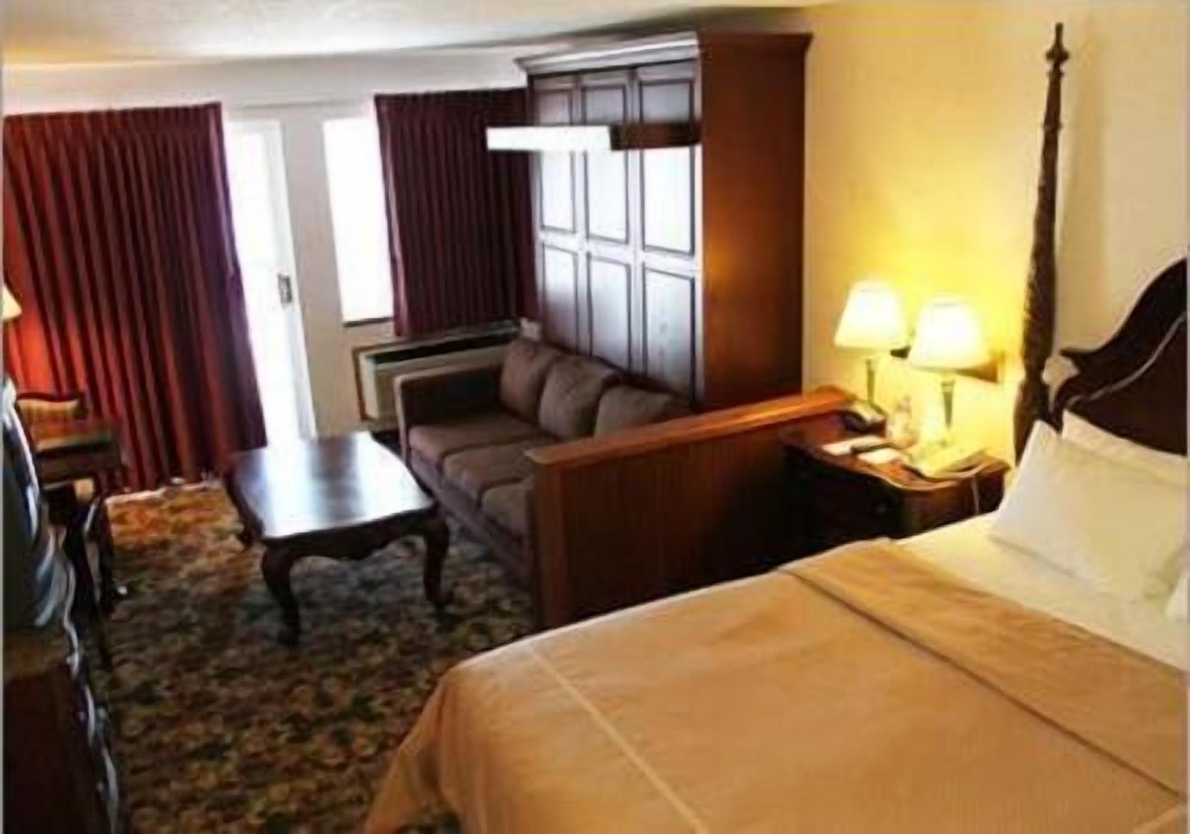 A hotel room with a bed, a sofa, a desk, and a nightstand with lamps.
