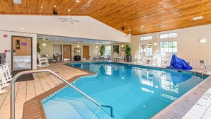 Una piscina interior con techo de madera, paredes de vidrio transparente y varias zonas de descanso.