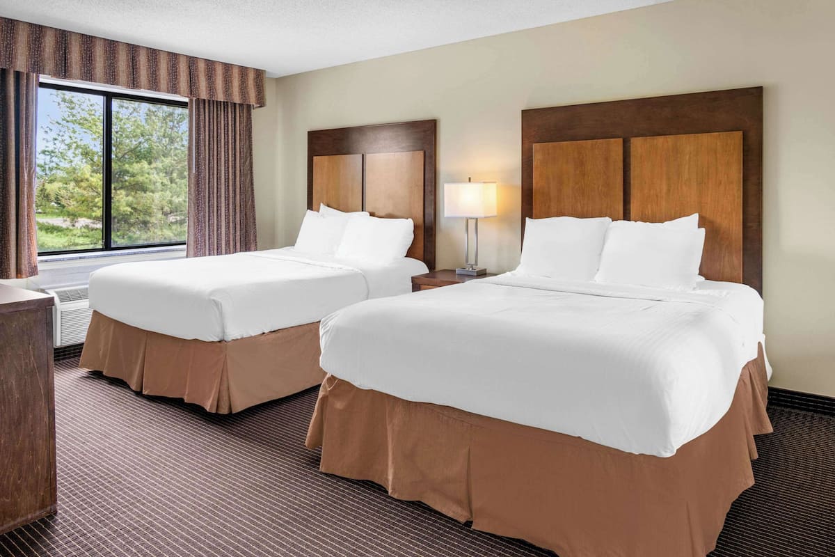 A hotel room with two beds, a window with curtains, a lamp, and a wooden headboard.