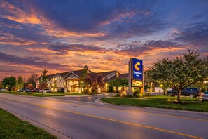 A hotel with a prominent sign, multiple buildings, and a road with parked cars. - Comfort Inn Holland (Holland)