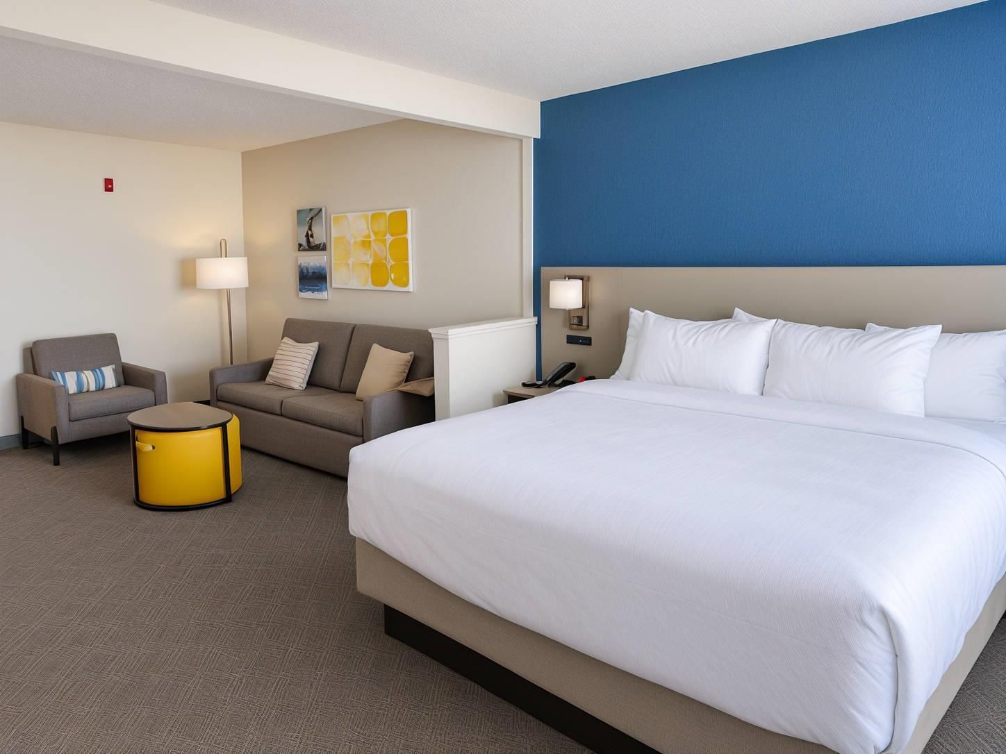 A hotel room with a large bed, two sofas, a small table, and a lamp.