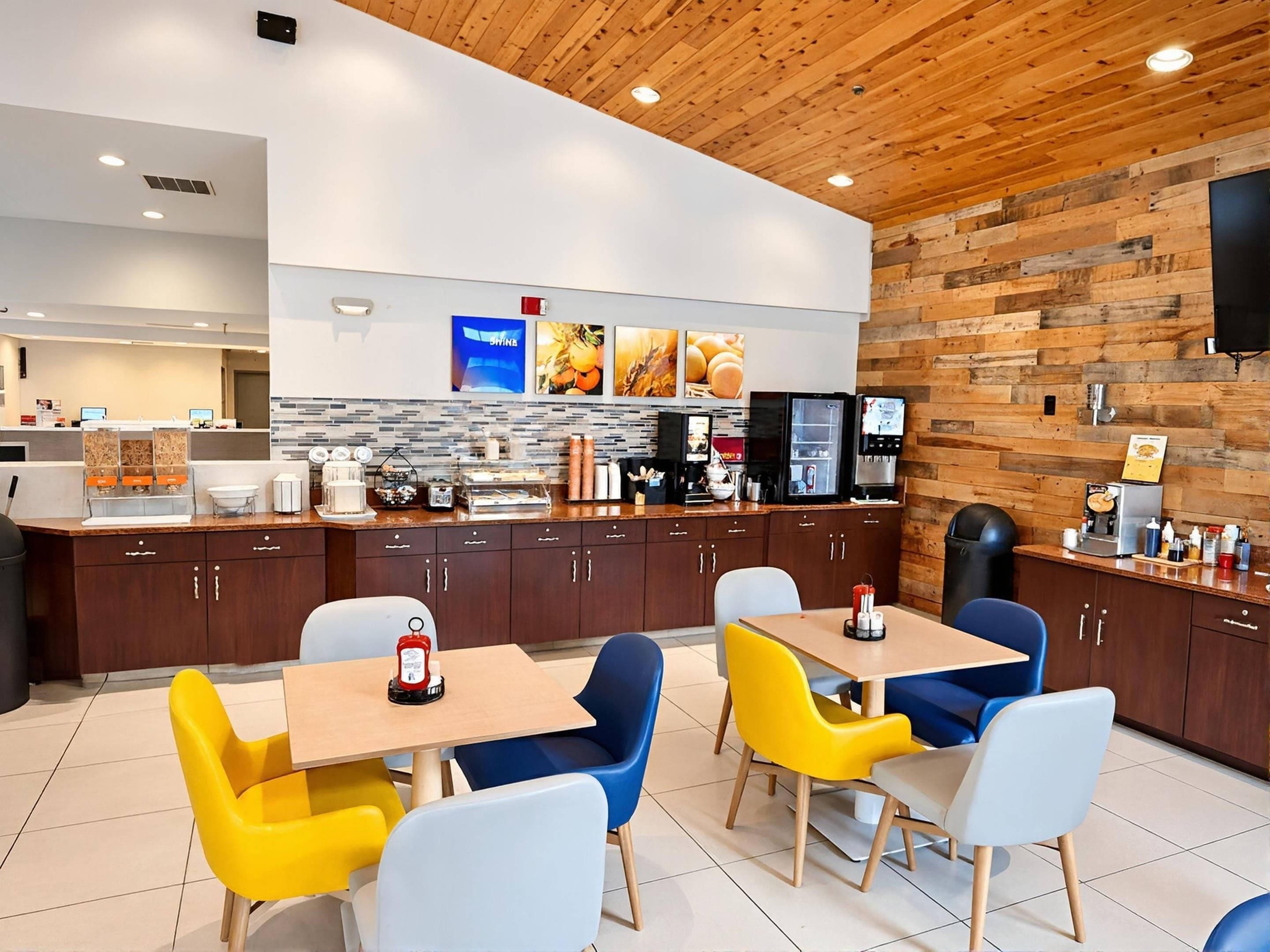 A modern restaurant with wooden ceiling and walls, a counter with a coffee machine, and colorful chairs.