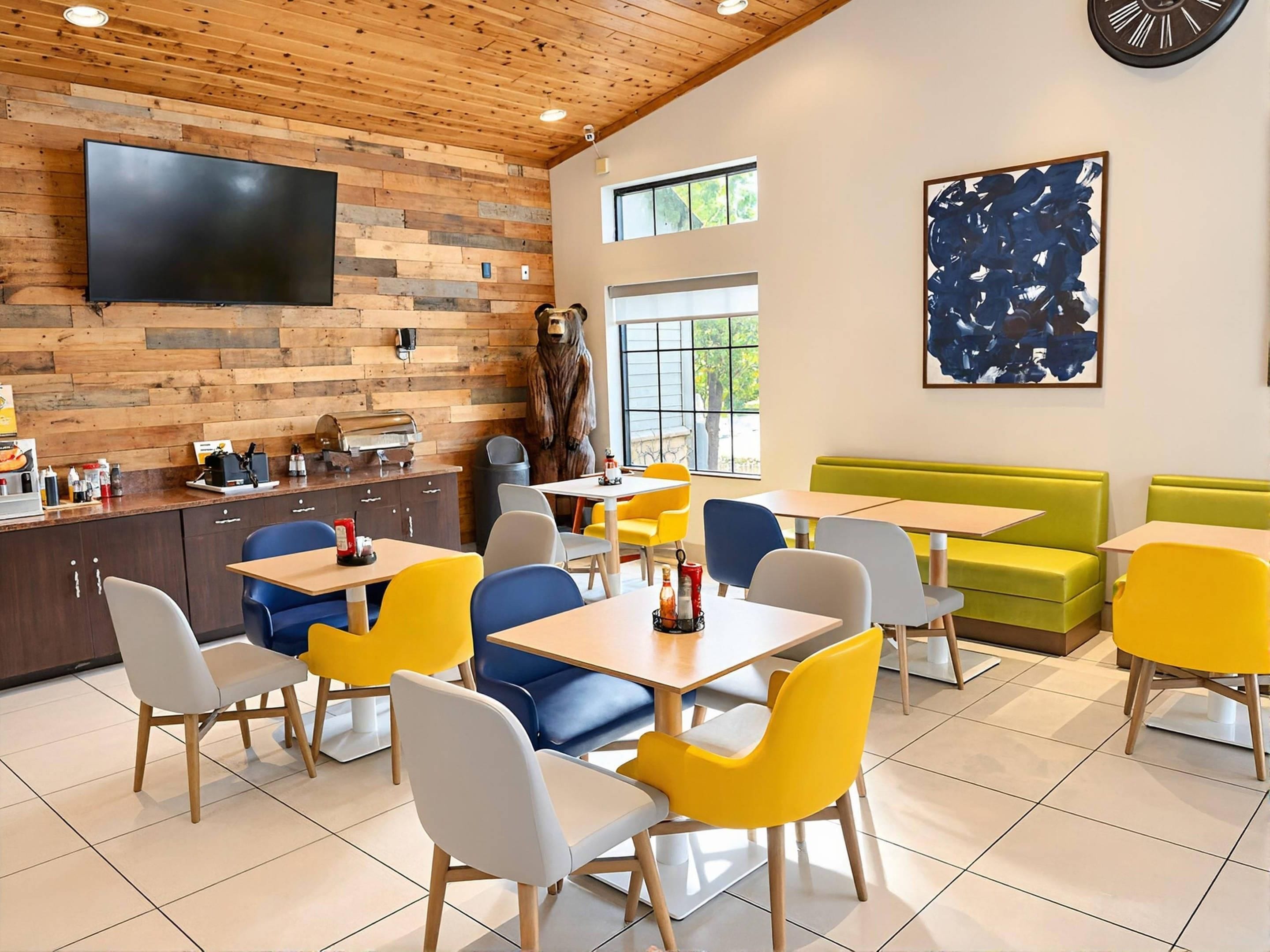 Un restaurant avec un mur en bois, une statue d’ours, des chaises jaunes et bleues, et un grand tableau abstrait.