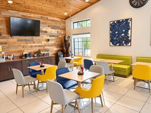 A restaurant with a wooden wall, a bear statue, yellow and blue chairs, and a large abstract painting. - Comfort Inn Holland (Holland)