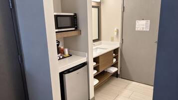 A compact bathroom with a microwave, sink, and storage shelves.