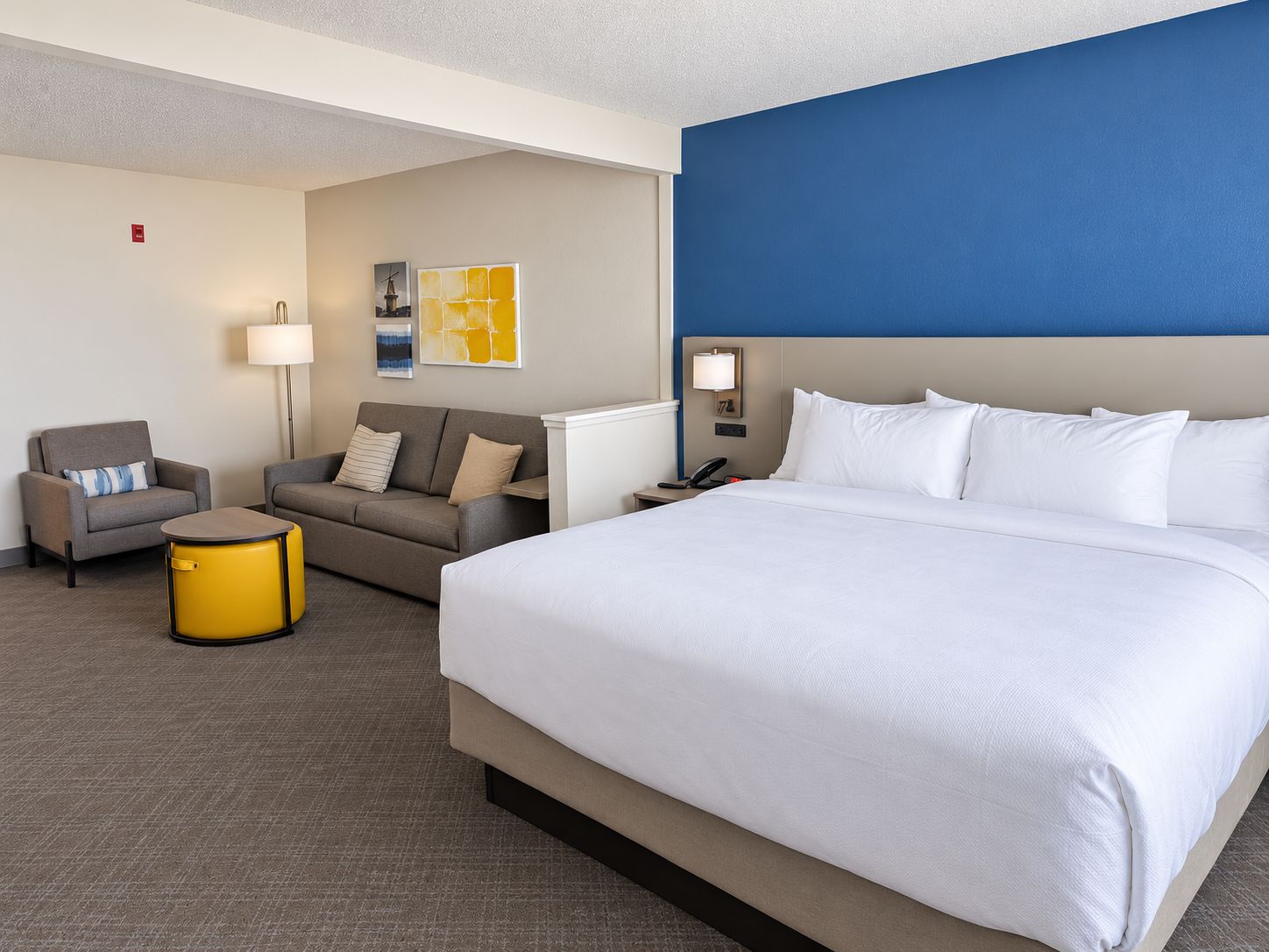 A hotel room with a large bed, a sofa, a small round table, and a lamp.