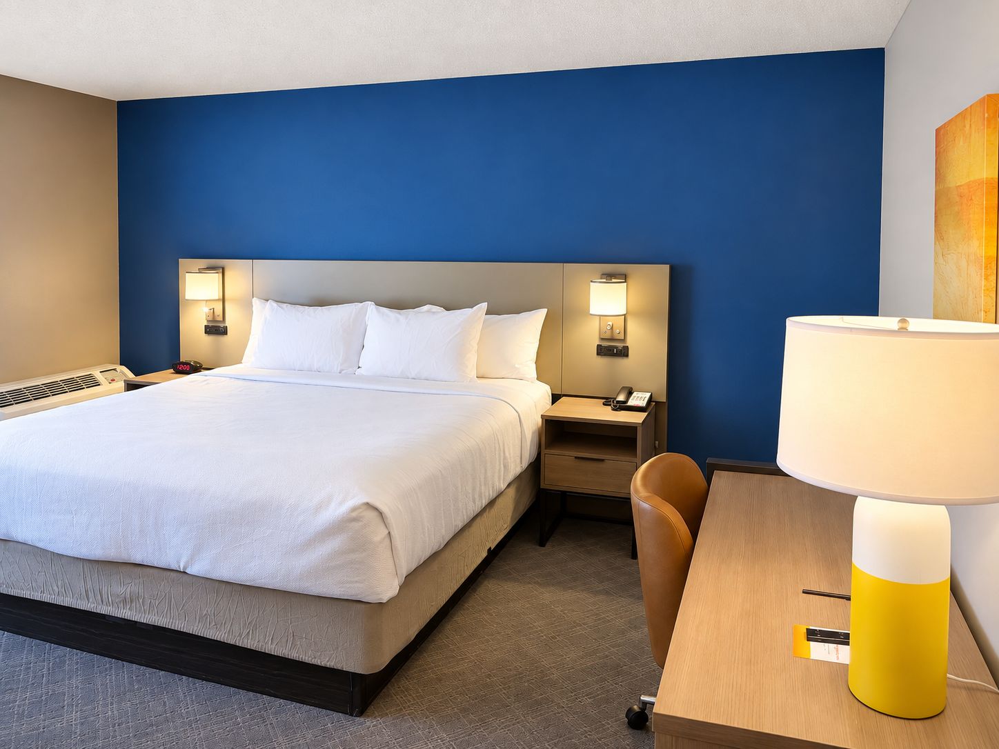 Ett hotellrum med en säng, sängbord, ett skrivbord och en lampa.