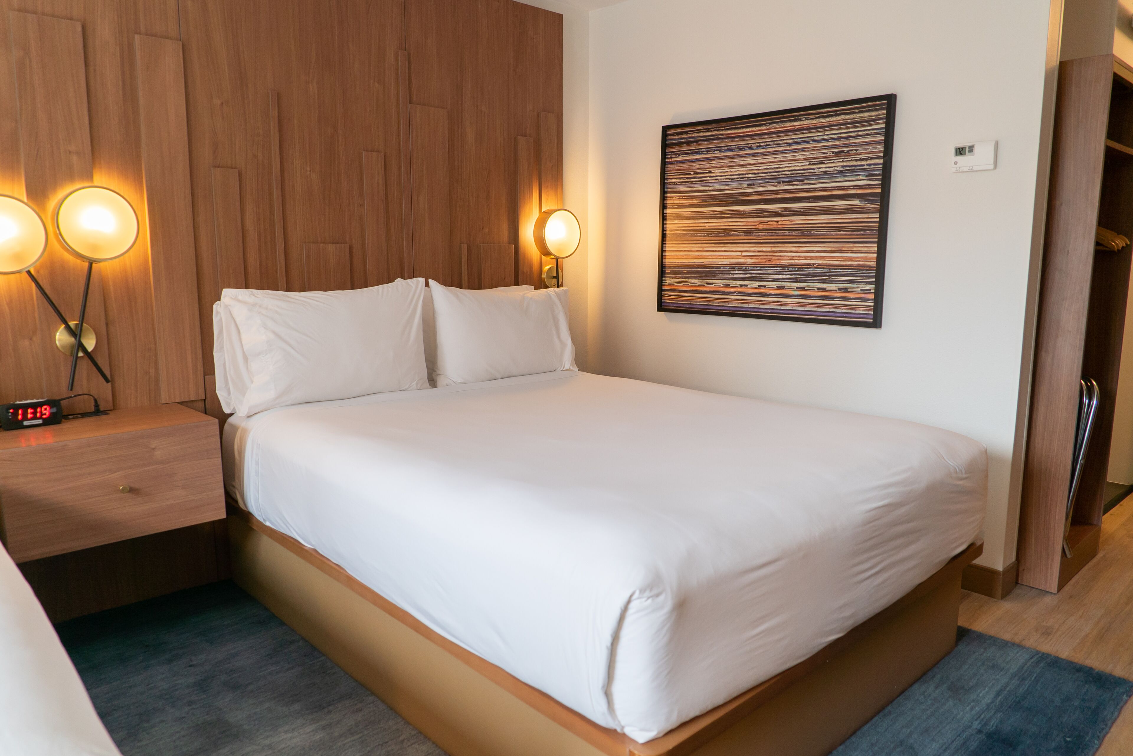 A neatly made bed with white linens, a wooden headboard, and two bedside lamps.
