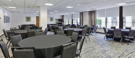 Una sala de conferencias con varias mesas y sillas, ventanas amplias y piso alfombrado.