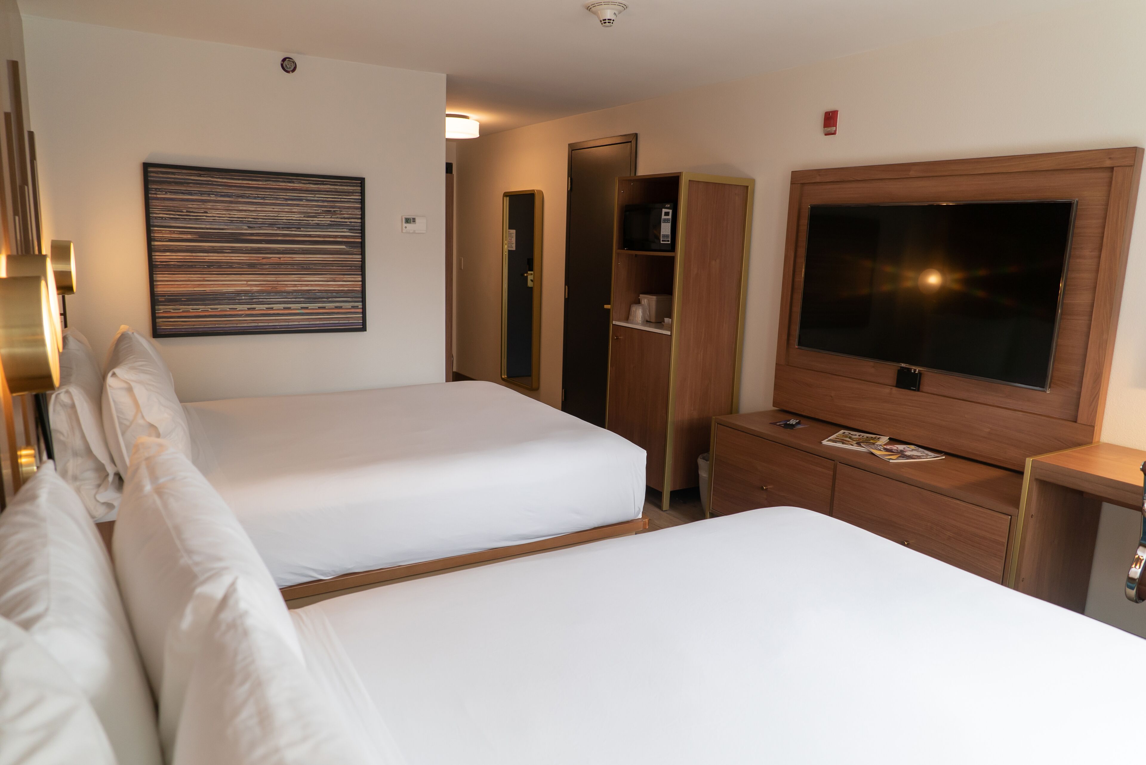 A hotel room with two beds, a TV, a wardrobe, and a painting on the wall.