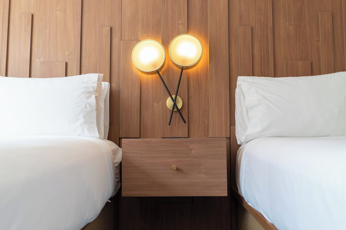Une chambre d’hôtel avec deux lits, une tête de lit en bois et une table de chevet avec un tiroir.