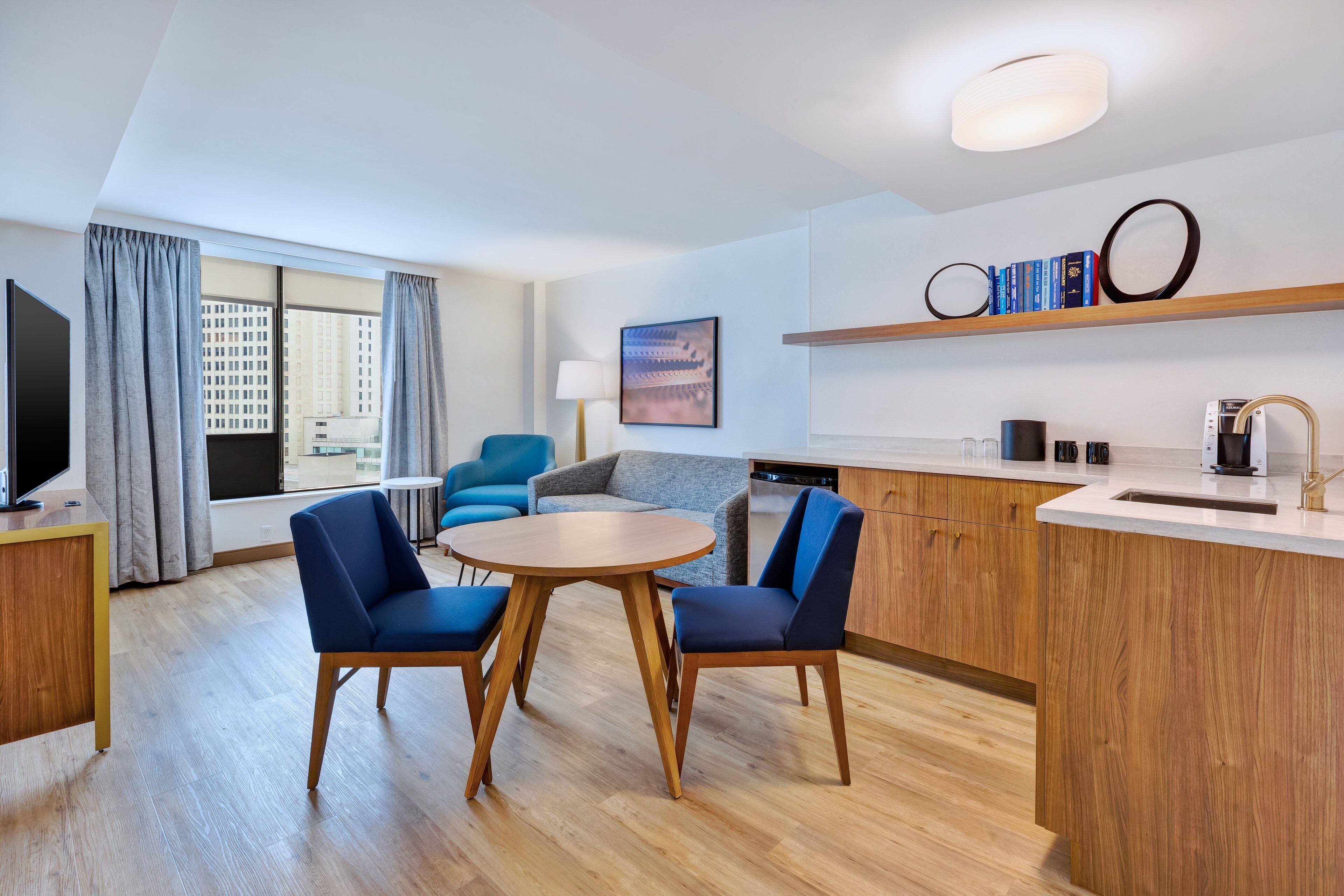 Une chambre d’hôtel moderne dotée d’un coin repas, d’un canapé, d’une télévision et offrant une vue sur la ville.
