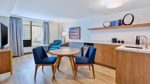 A modern hotel room with a dining area, a sofa, a TV, and a view of the city. - Hotel Indigo Detroit Downtown by IHG (Detroit)