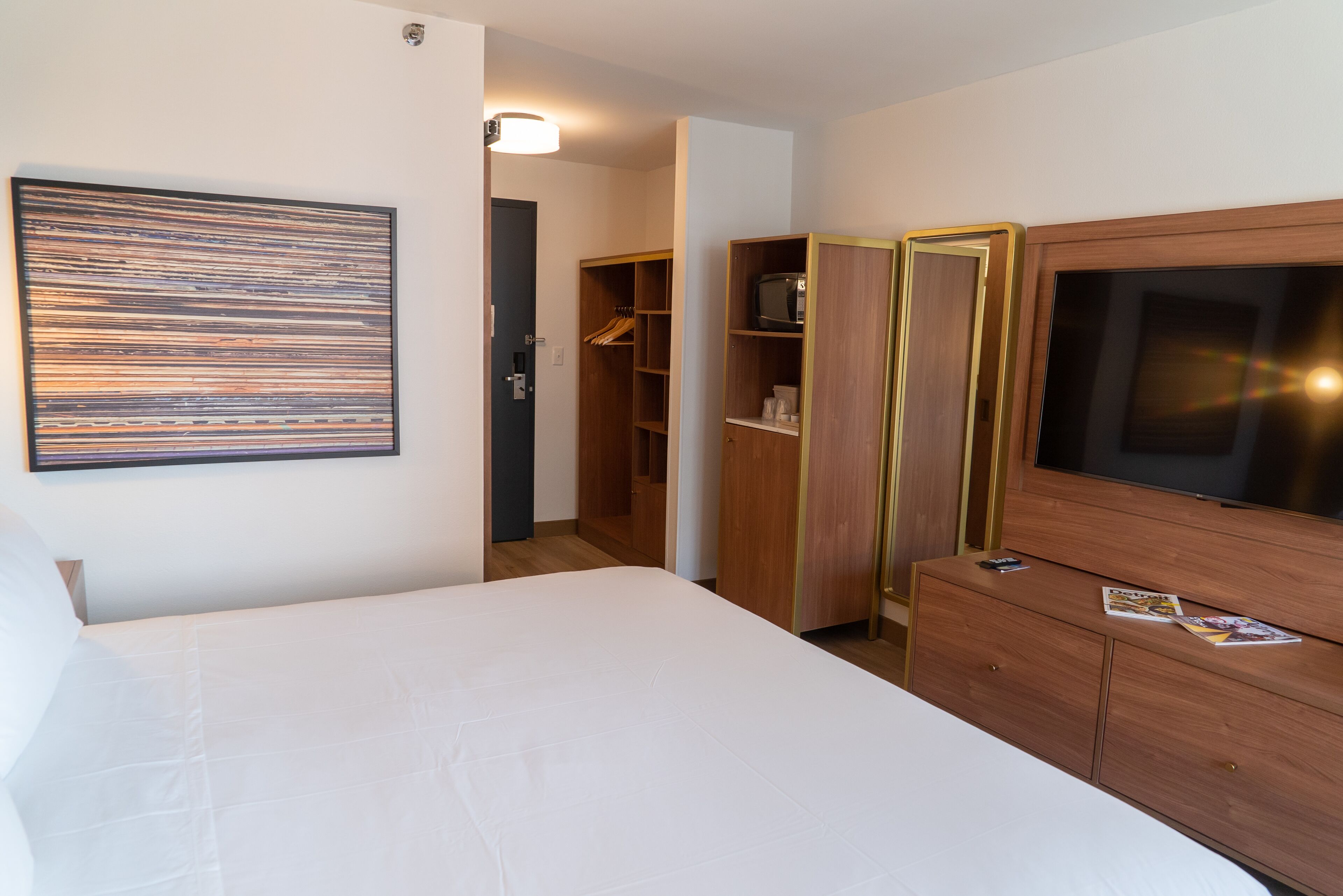 A hotel room with a large bed, a wardrobe with a television, and a closet with shelves.