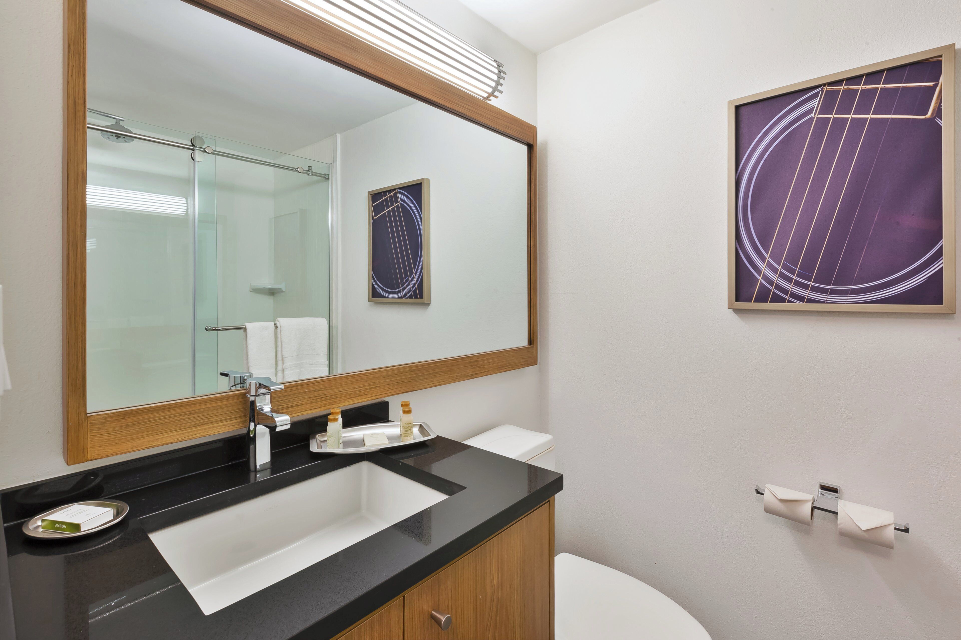 A bathroom with a large mirror, a sink, a toilet, and a framed artwork on the wall.