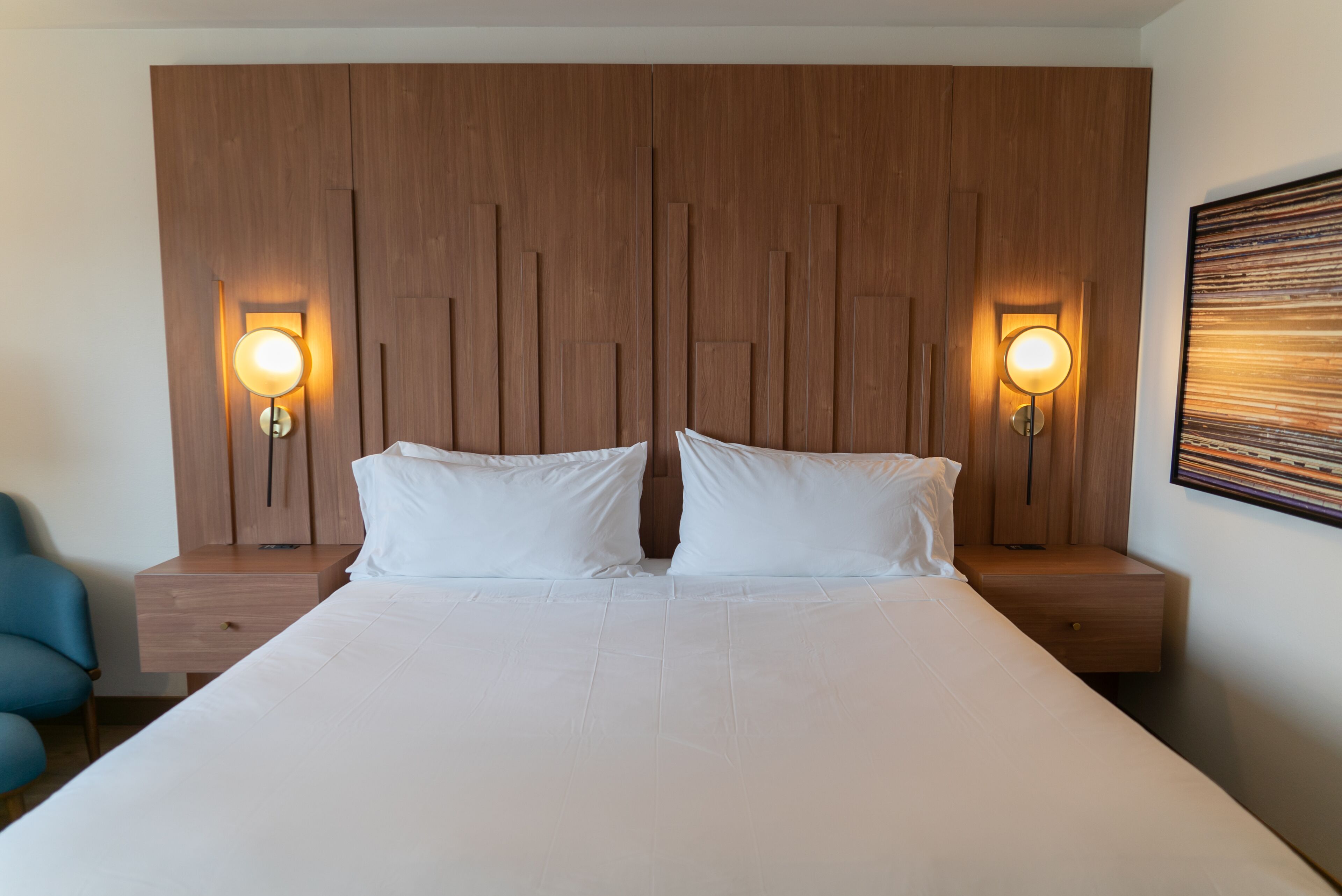 A hotel room with a large bed, two bedside tables, and two wall-mounted lamps.