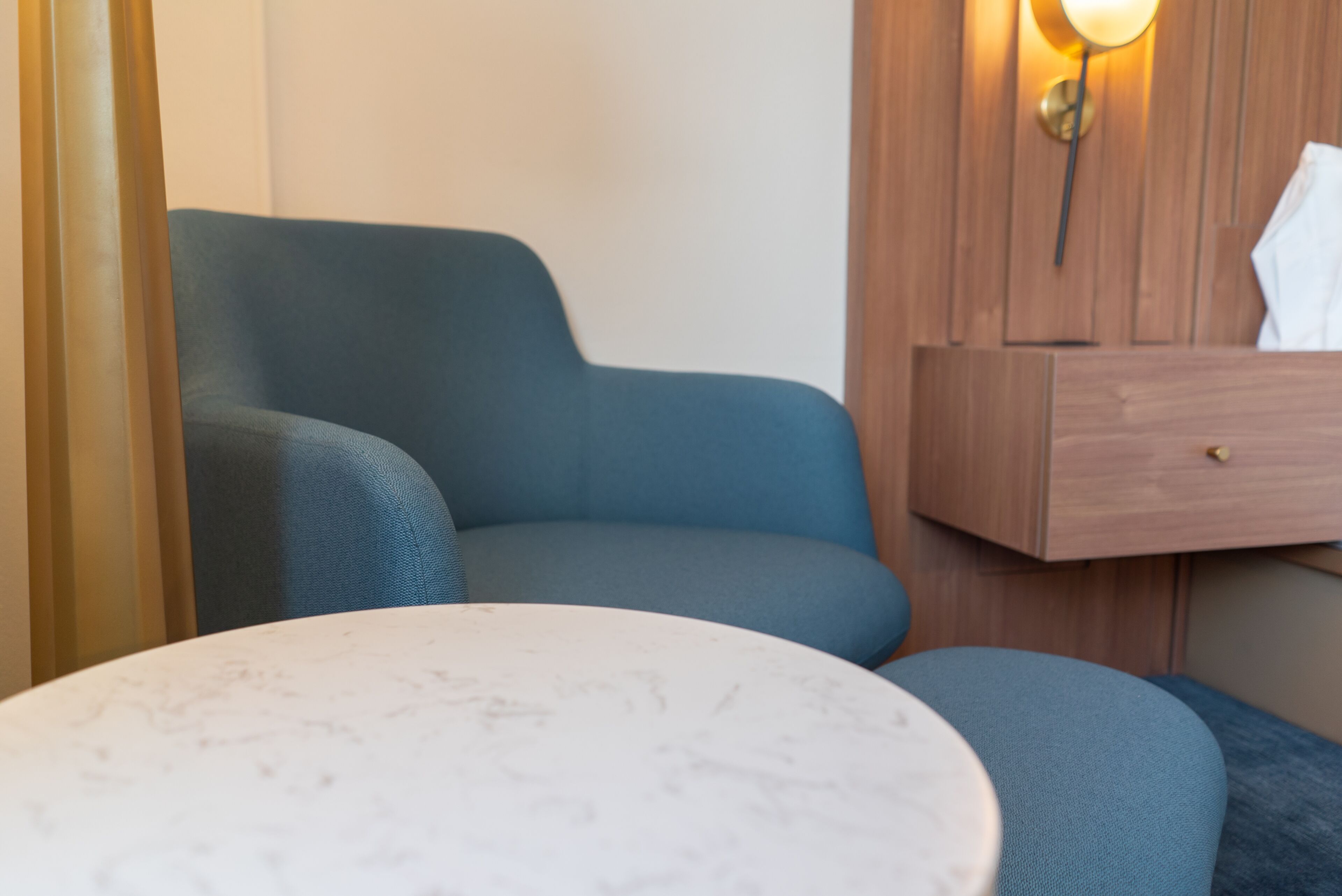 A room with a blue armchair, a wooden nightstand with a lamp, and a marble table.