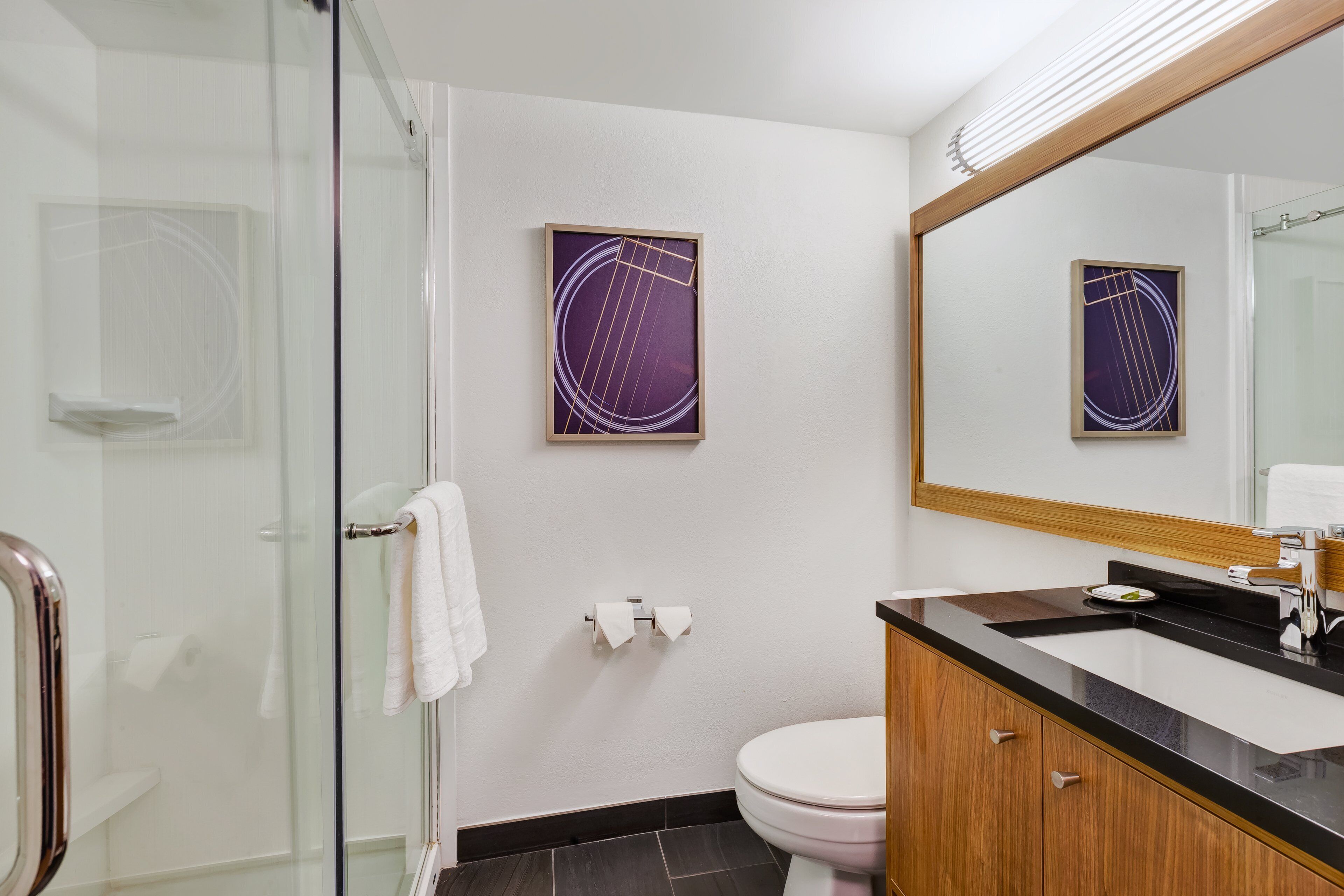 Une salle de bain moderne avec une douche à parois de verre, des toilettes blanches et un lavabo noir avec un meuble en bois.