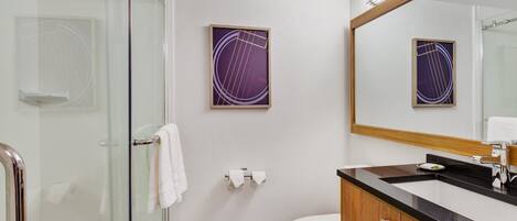 Un baño moderno con cabina de ducha de vidrio, inodoro blanco y lavamanos negro con gabinete de madera.