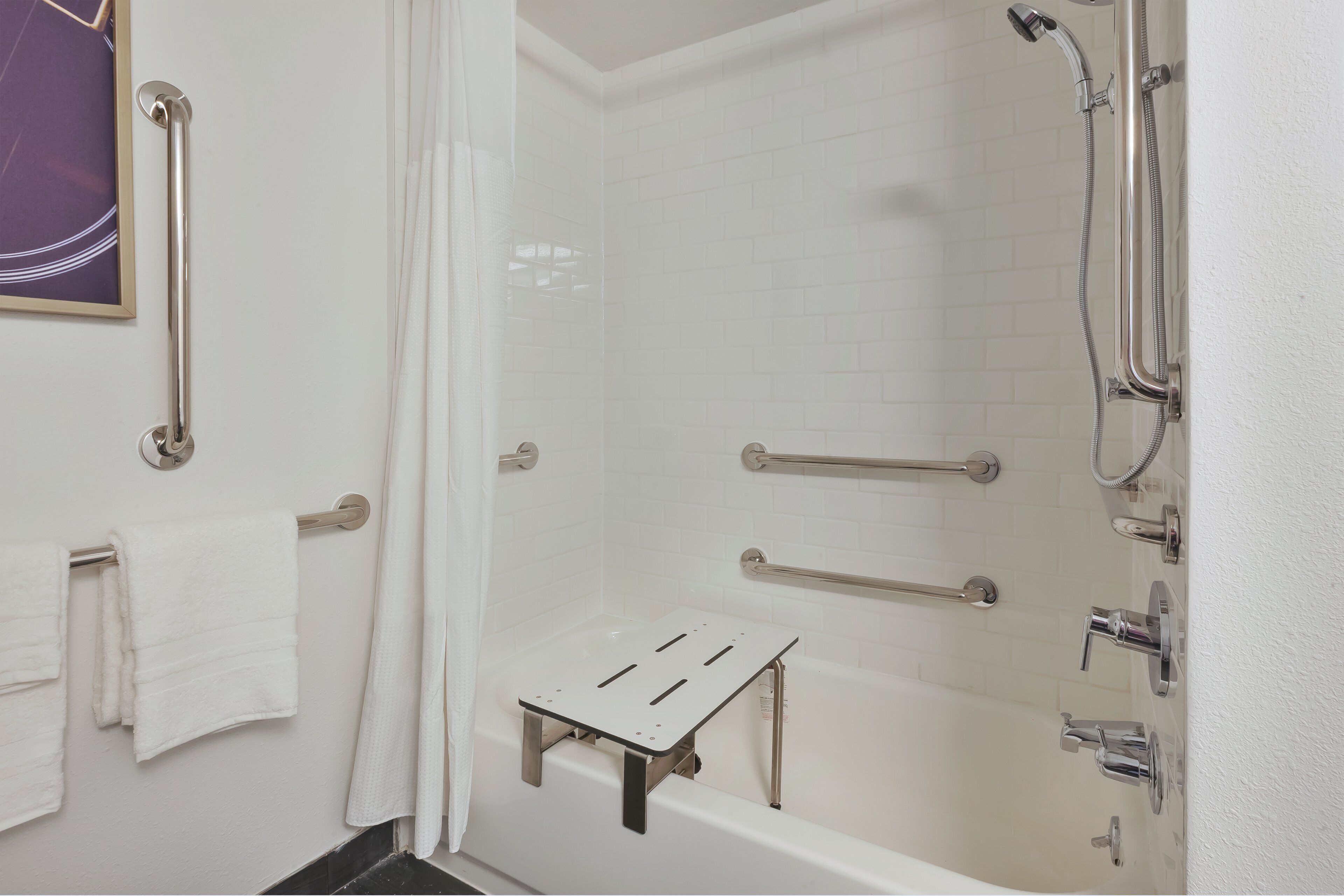 Une salle de bain avec une baignoire blanche, une douche équipée d’un pommeau de douche amovible et de barres d’appui pour plus de sécurité.