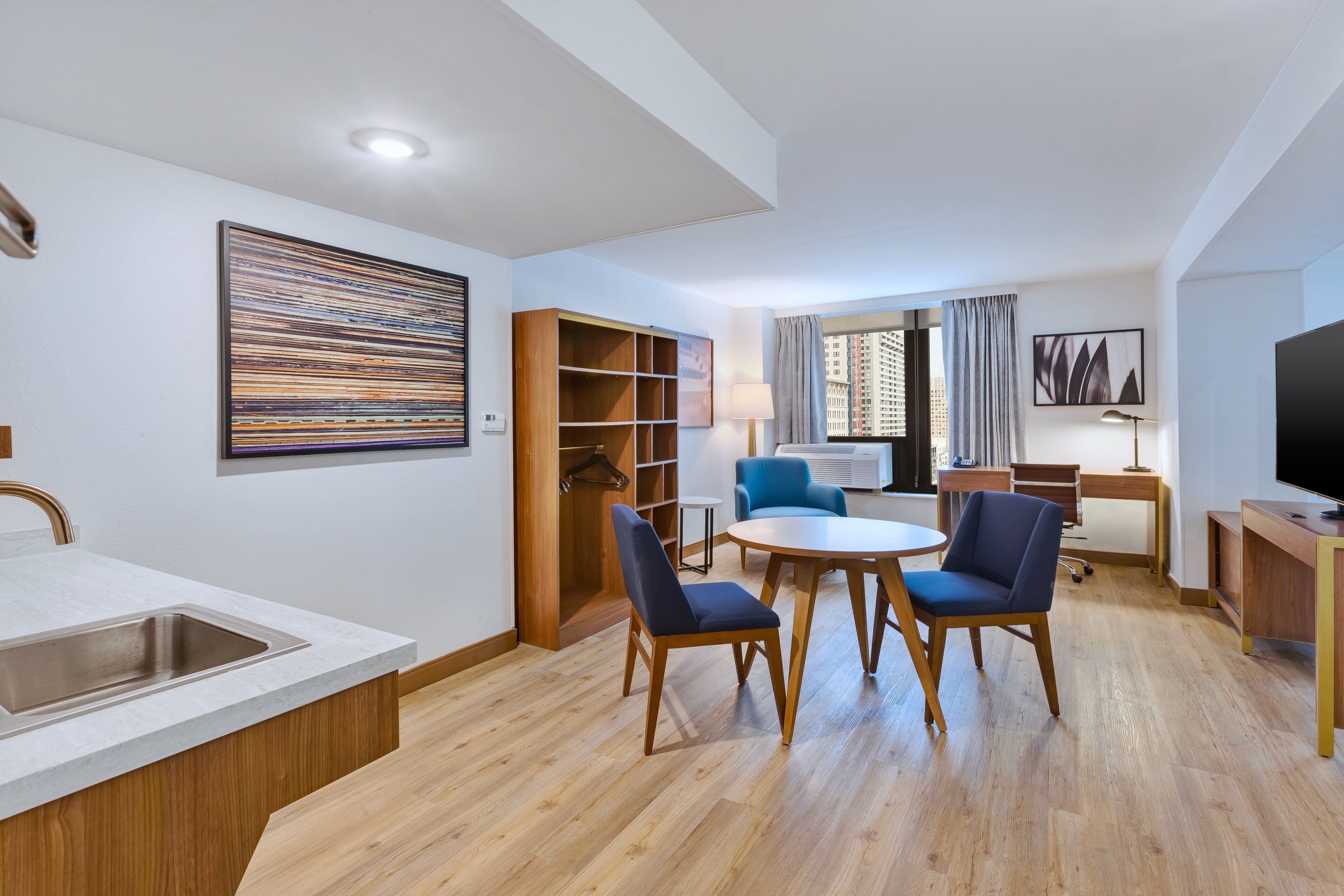 A modern hotel room with a kitchen area, dining table, and seating.