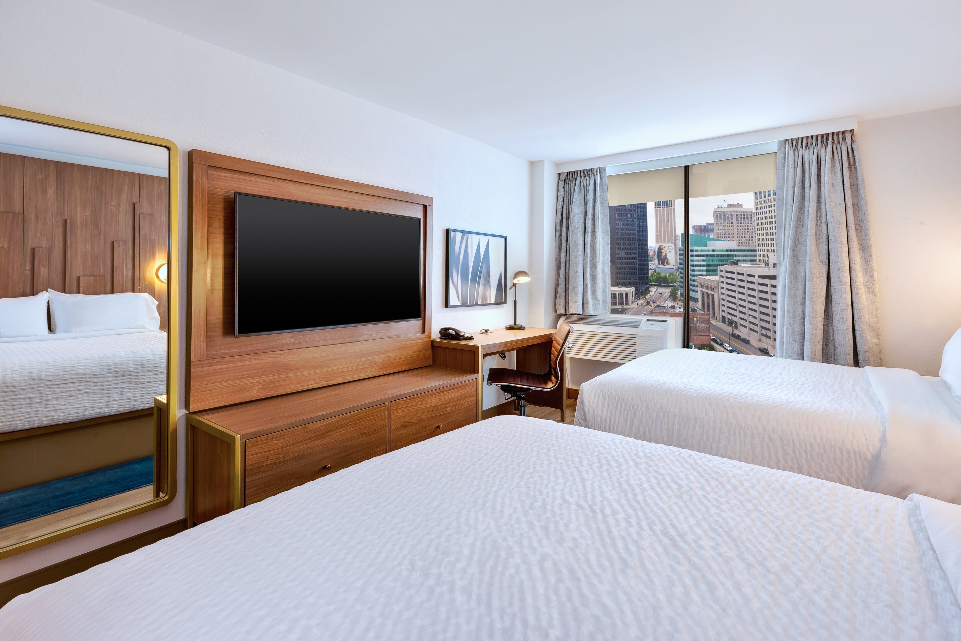 Une chambre d’hôtel avec deux lits, un bureau avec une chaise, une télévision et une grande fenêtre avec des rideaux.