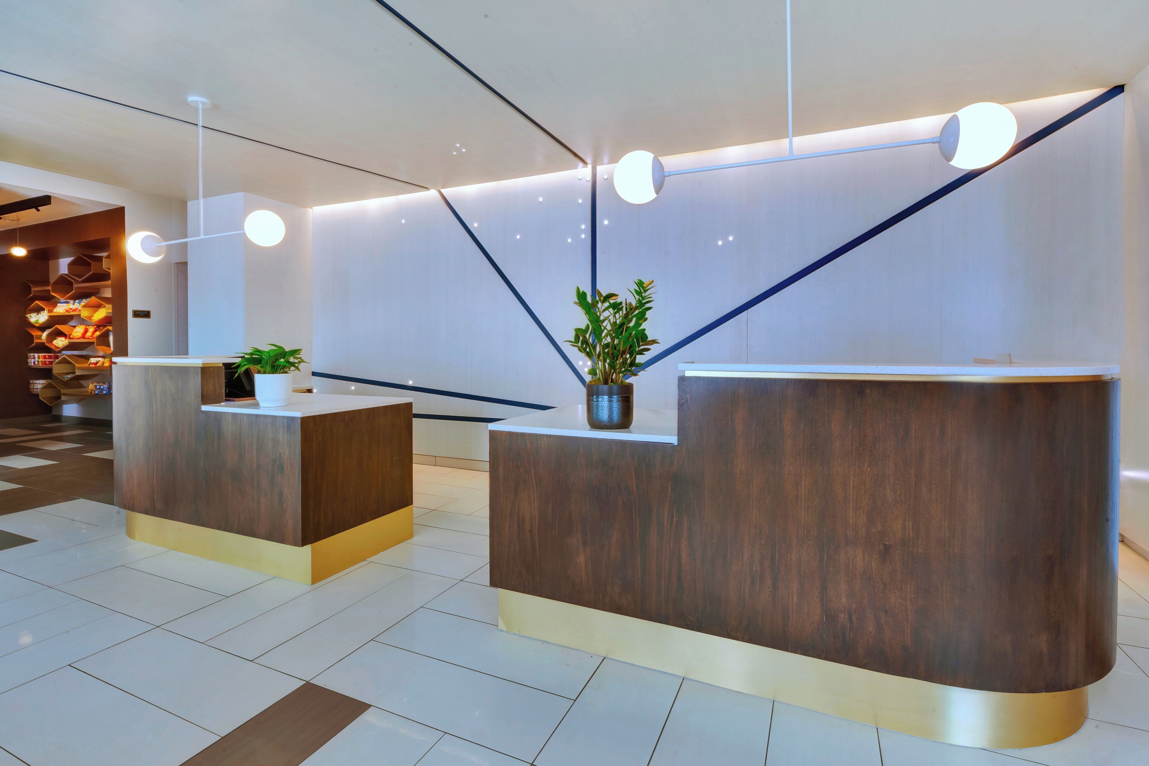 A reception area with two wooden reception desks, a potted plant, and a wall with recessed lighting.