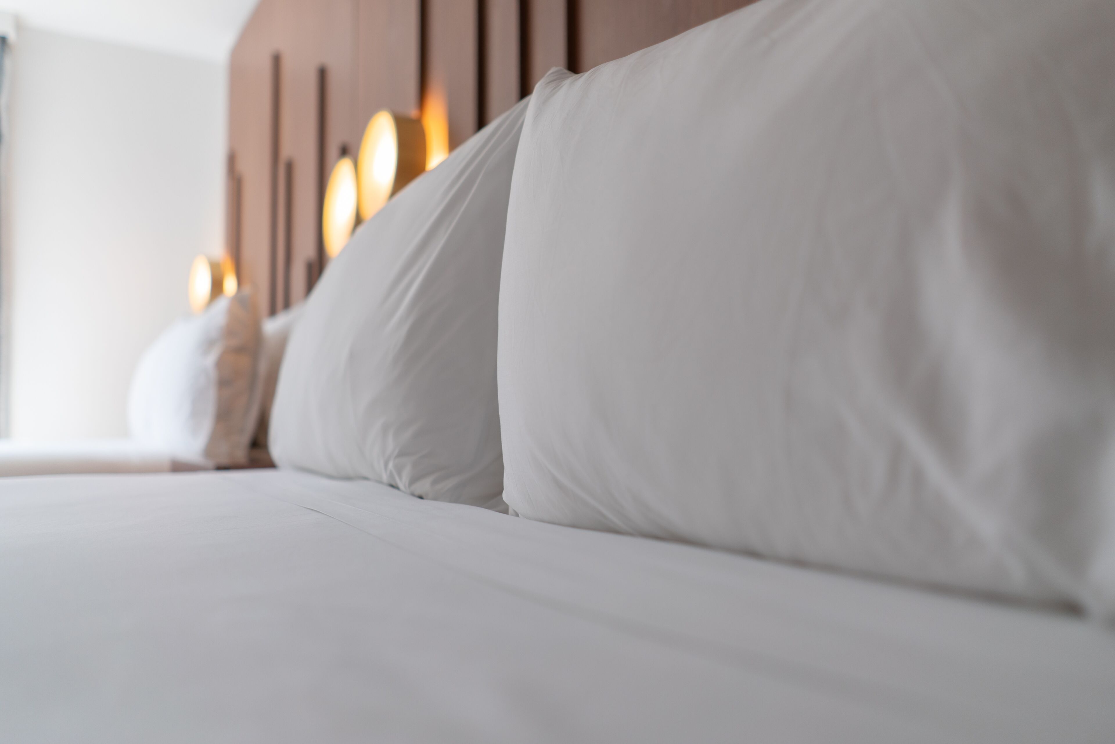 A close-up of a neatly made bed with white linens and a wooden headboard.