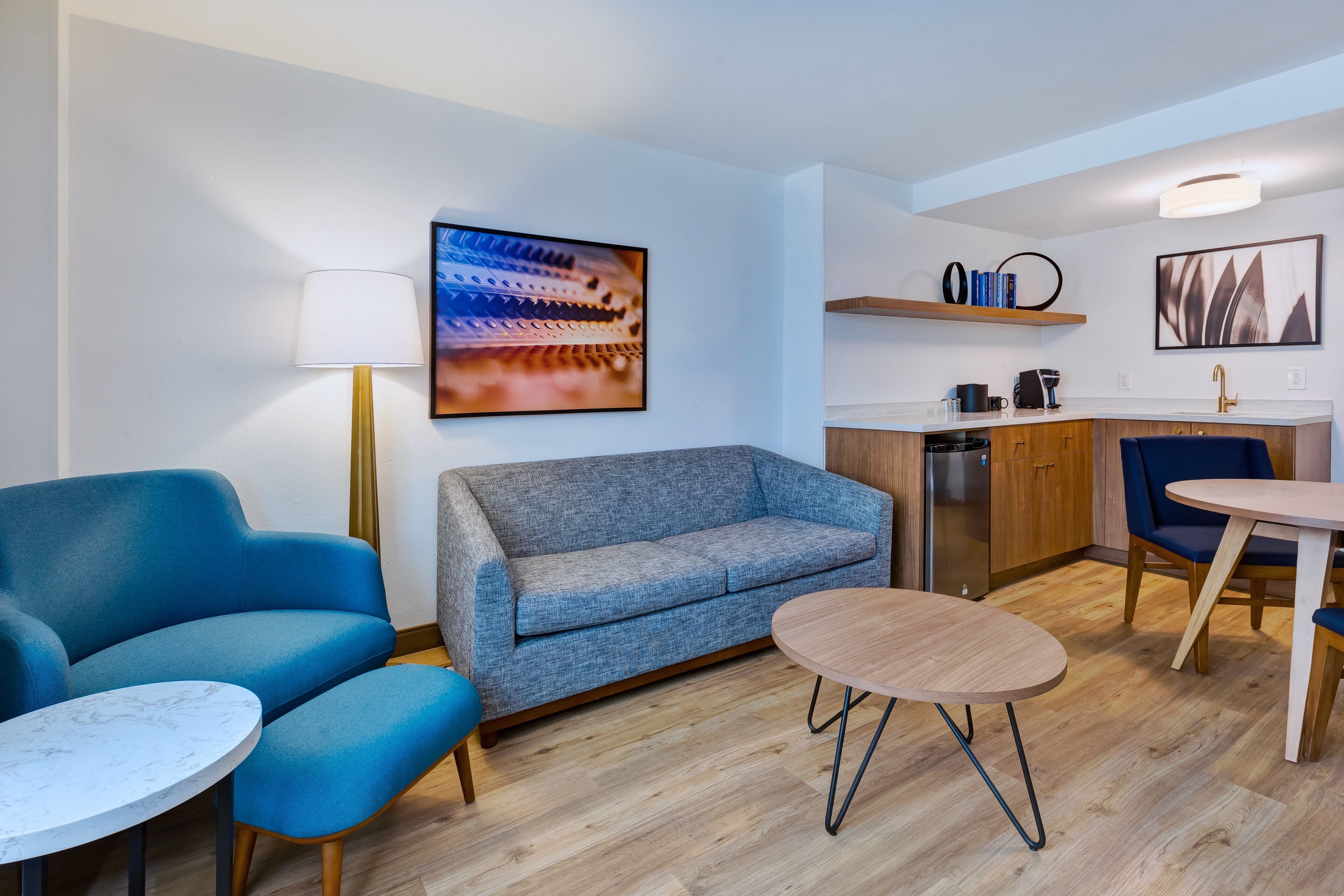 Ein modernes Wohnzimmer mit einer Couch, zwei Sesseln, einem kleinen Tisch und einer Küchenzeile mit Spüle und Arbeitsfläche.