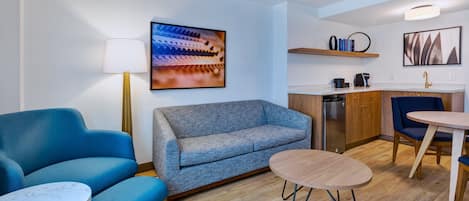 Una sala de estar moderna con un sofá, dos sillones, una mesita y una zona de cocina con un lavamanos y encimera.