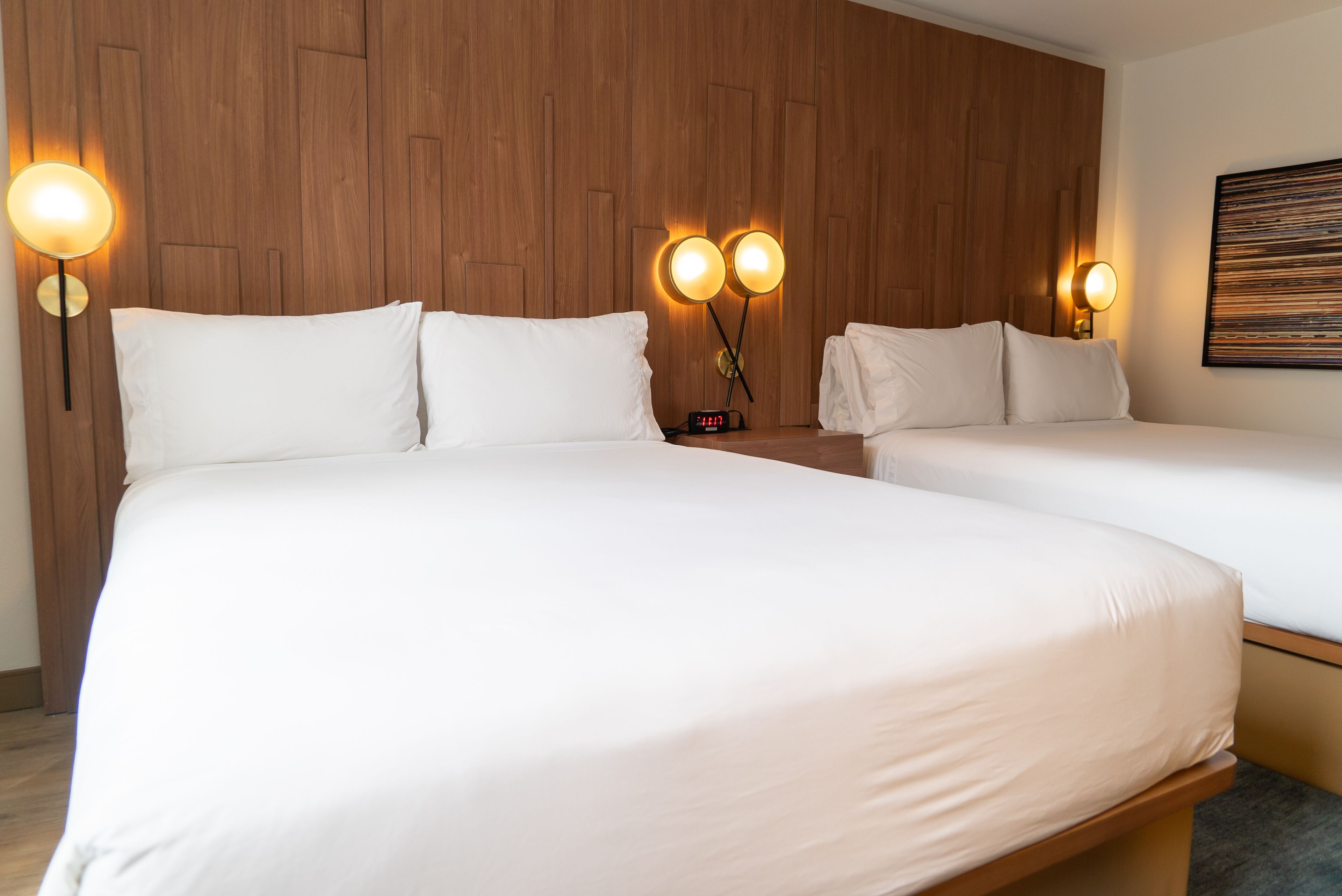 A hotel room with two beds, wooden panel walls, and wall-mounted lamps.