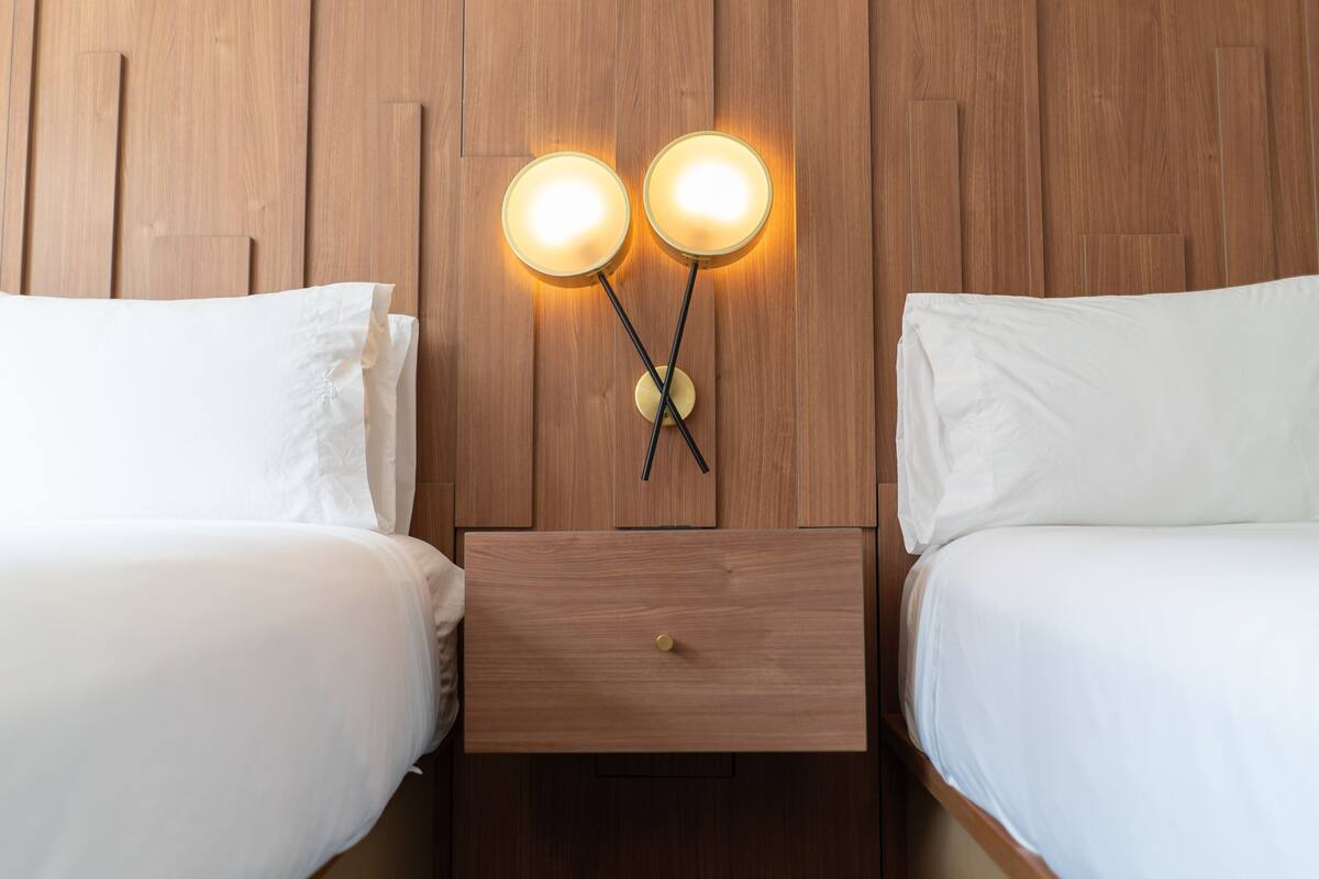 A hotel room with two beds, a wooden headboard, and a nightstand with a drawer.