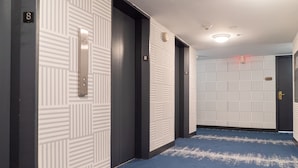 A hallway with patterned walls, numbered doors, and a blue carpet.