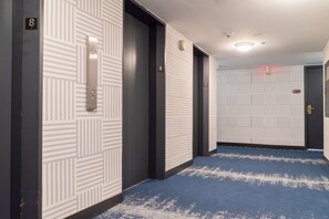 Un couloir aux murs ornés de motifs, avec des portes numérotées et un tapis bleu.