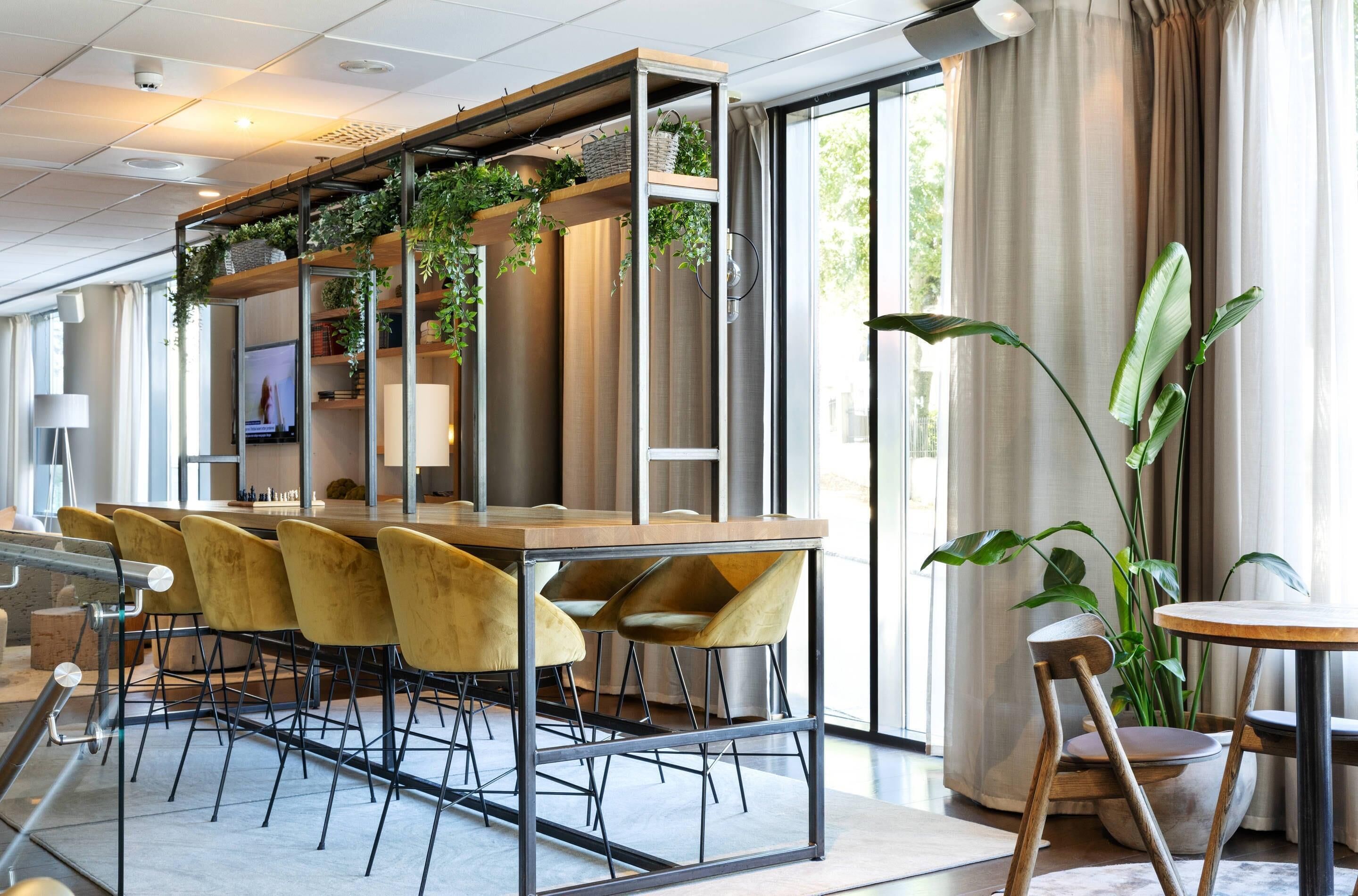 A modern bar area with a wooden counter, yellow bar stools, and a large potted plant.