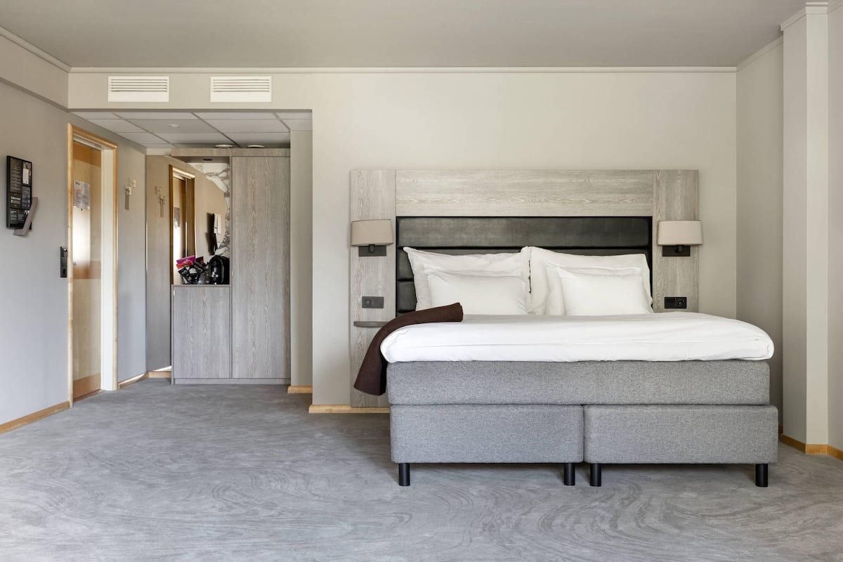 A modern hotel room with a large bed, a headboard, two bedside lamps, and a carpeted floor.