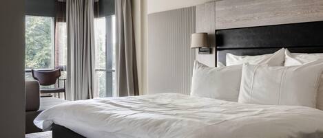 Habitación de hotel con una cama grande, una lámpara de noche, vistas al exterior y una silla junto a la ventana.