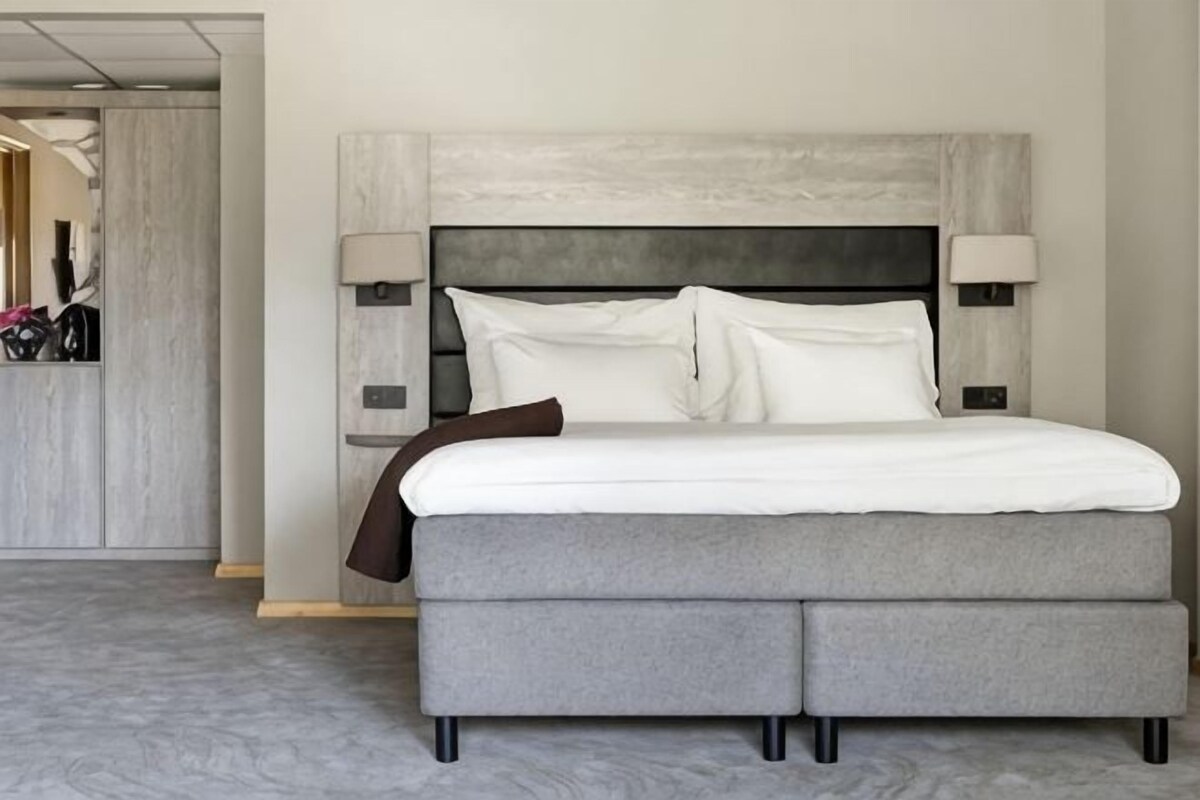 A modern hotel room with a large bed, a headboard with integrated lighting, and a neutral color palette.