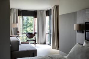 Una habitación de hotel con cama, una silla, un escritorio y un ventanal con cortinas.